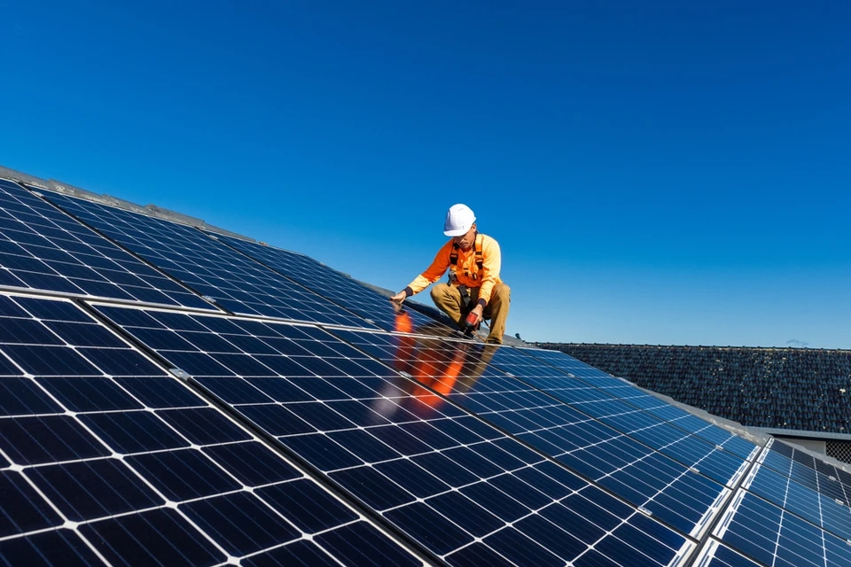 Technicien en équipement de protection individuelle installant des panneaux solaires photovoltaïques sur toiture résidentielle par temps ensoleillé
