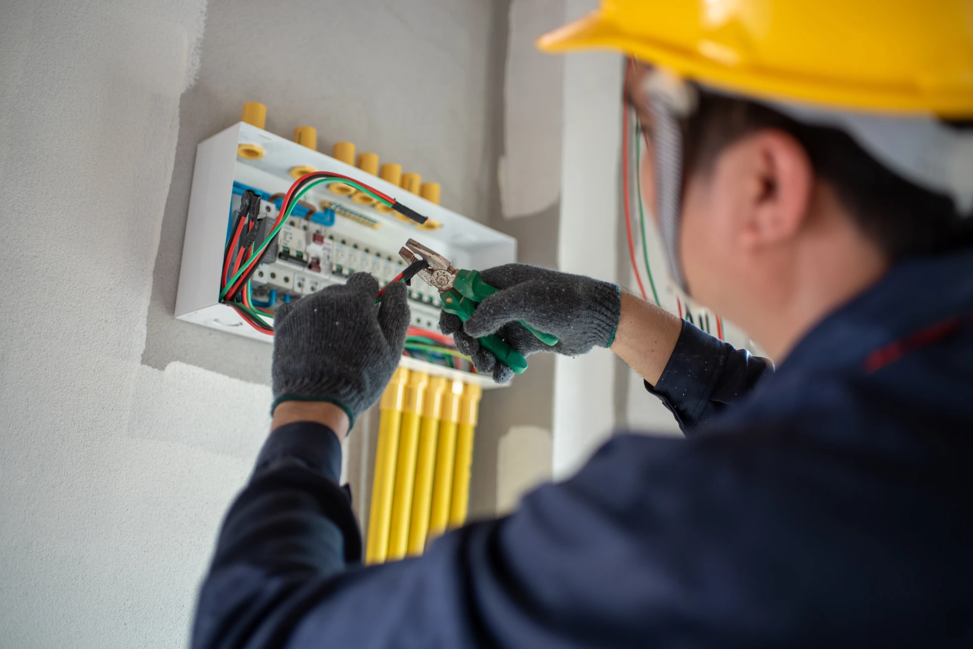 Un électricien en casque jaune travaille sur un tableau électrique mural