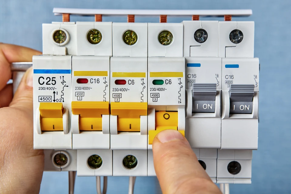 Intérieur, mains manipulant un tableau électrique, doigt appuyant sur un disjoncteur différentiel jaune en position test