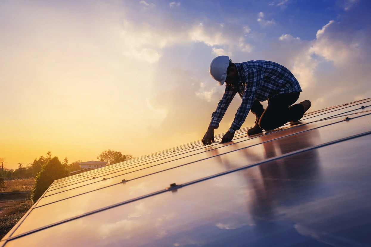 Ouvrier installateur en combinaison et casque de protection travaillant sur toiture, manipulant des panneaux photovoltaïques solaires