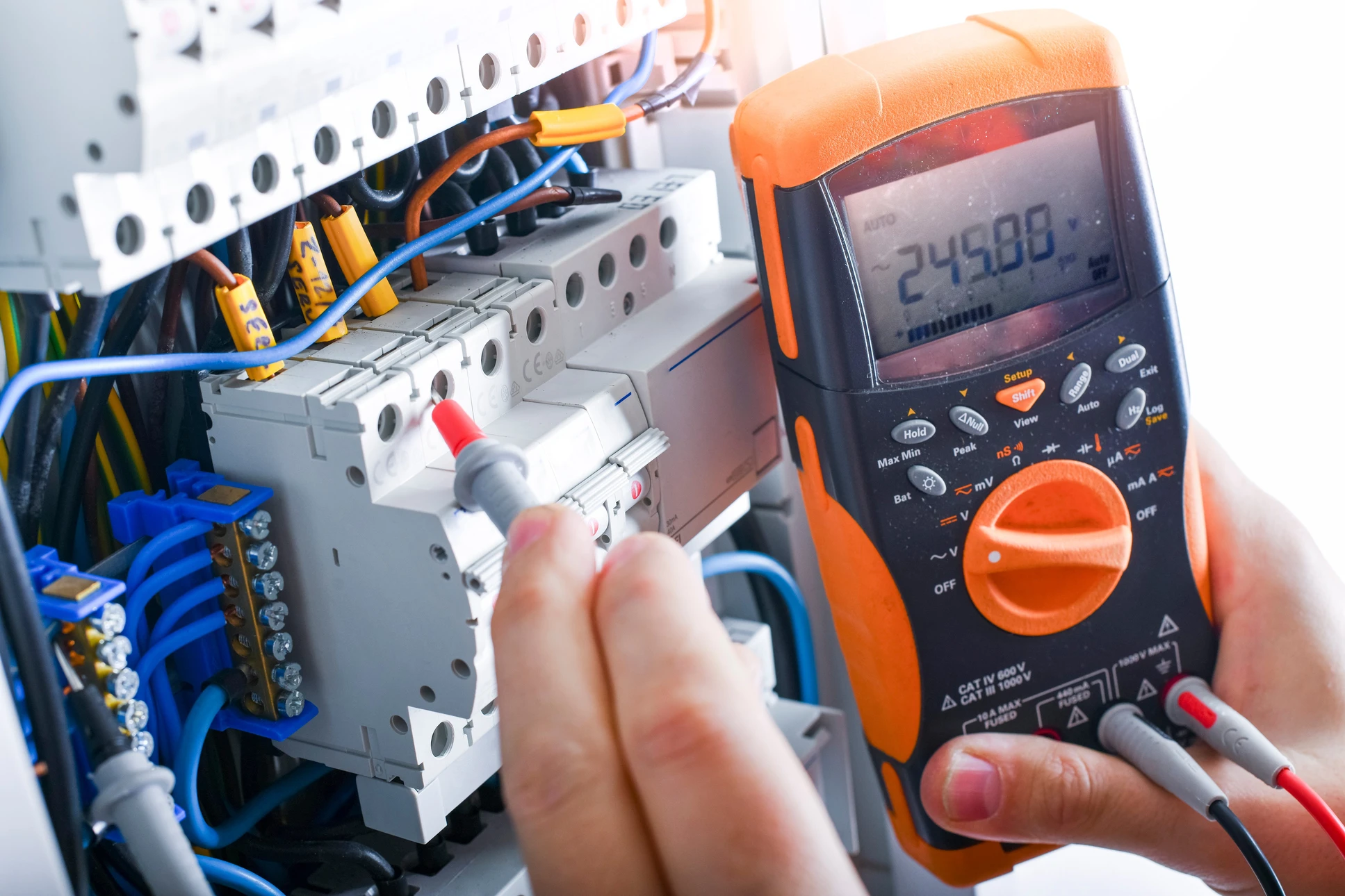 Électricien en tenue bleue effectuant des mesures électriques sur installation murale avec multimètre numérique orange