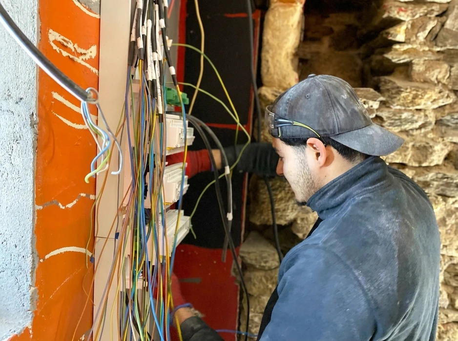 Électricien en casquette et lunettes de protection travaille sur un tableau électrique mural encadré de rouge