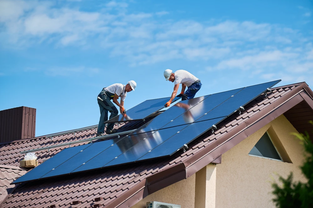 Deux techniciens en tenue de travail et casques de protection installent des panneaux solaires photovoltaïques sur une toiture résidentielle par temps ensoleillé