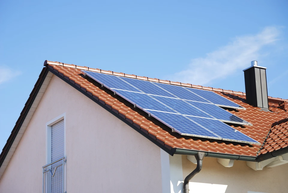Deux professionnels sur un toit analysent des donn&eacute;es sur tablette num&eacute;rique pr&egrave;s d'une installation de panneaux solaires photovolta&iuml;ques