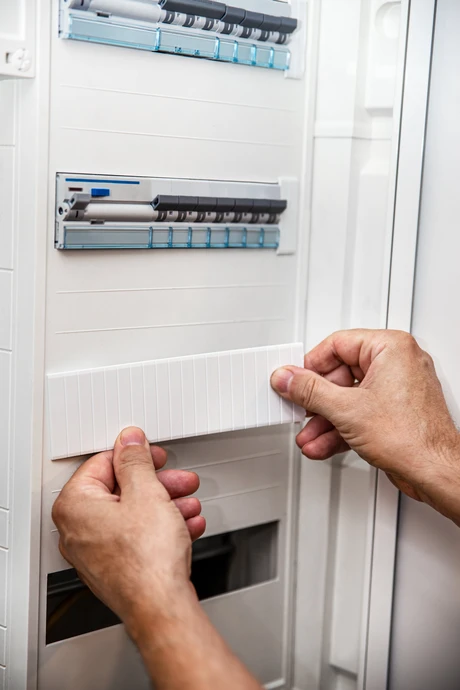 Électricien en salopette et casque jaune travaillant à l'intérieur d'un bâtiment, utilisant un multimètre pour tester une installation électrique