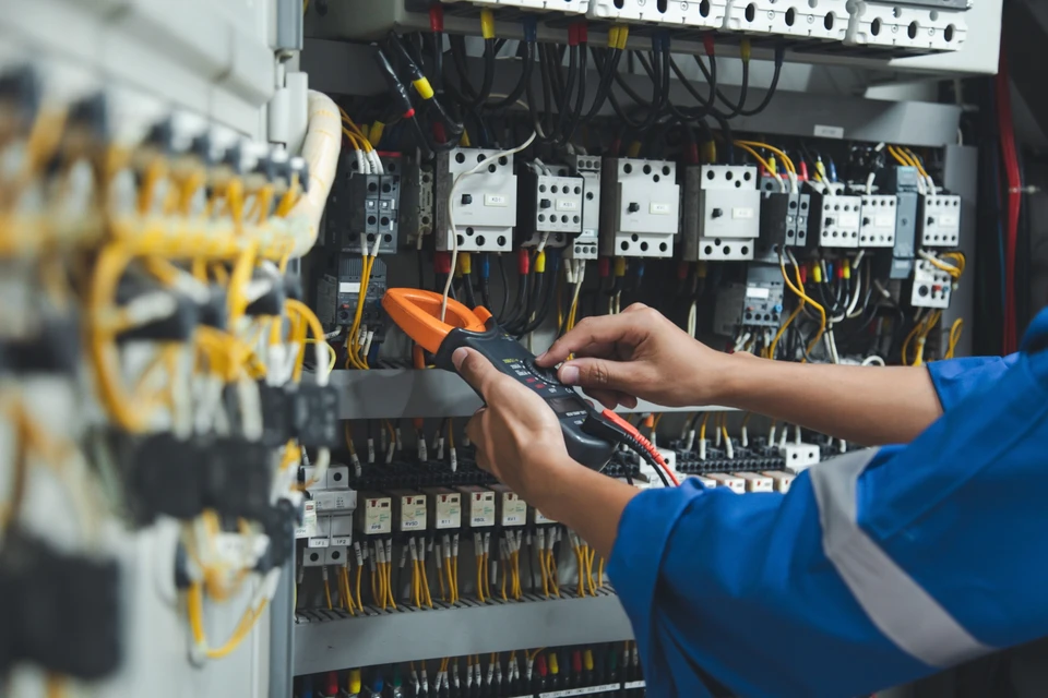 Un électricien masculin professionnellement vêtu, en train de diagnostiquer ou de réparer un panneau électrique/disjoncteur dans une maison d'habitation. L'électricien doit être muni d'outils (tournevis, multimètre ou testeur électrique) et en action, montrant l'engagement et la réactivité d'une intervention d'urgence. La scène doit être réaliste, en intérieur résidentiel, avec un bon éclairage, transmettant la compétence et la disponibilité du professionnel.
