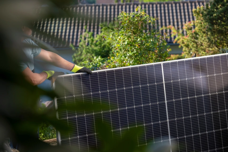 Technicien installant des panneaux solaires photovolta&iuml;ques sur toiture r&eacute;sidentielle sous ciel bleu