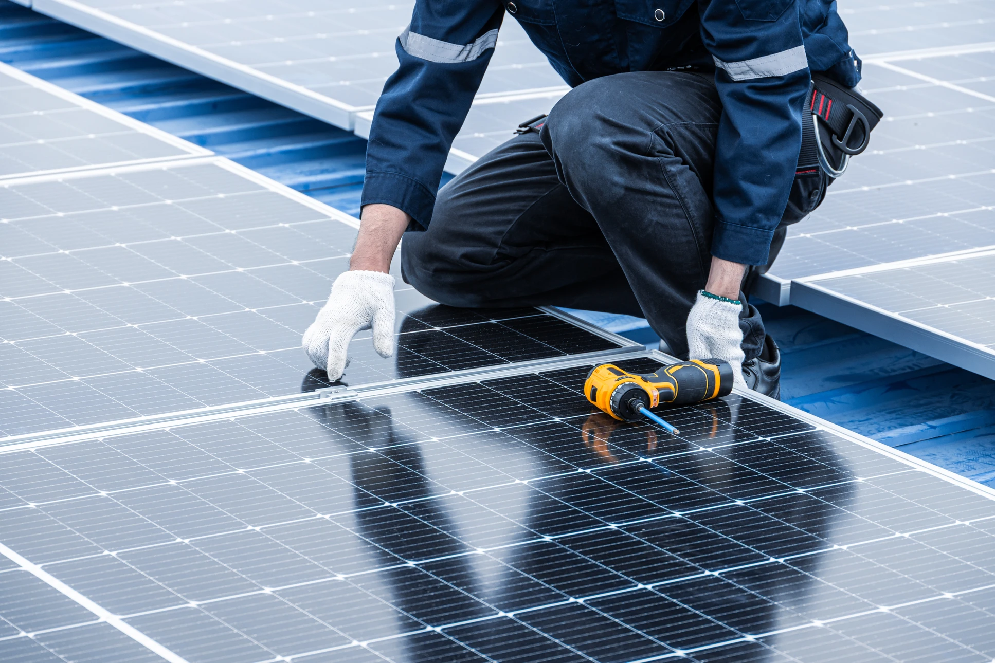 Technicien en équipement de sécurité installant des panneaux photovoltaïques sur toiture résidentielle sous ciel bleu dégagé
