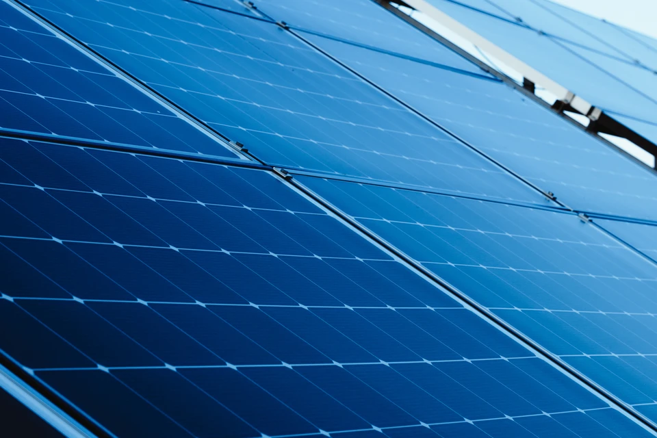 Ouvrier en tenue de sécurité haute visibilité et casque jaune installant des panneaux solaires photovoltaïques sur toiture résidentielle en bardeaux rouges, ciel bleu dégagé